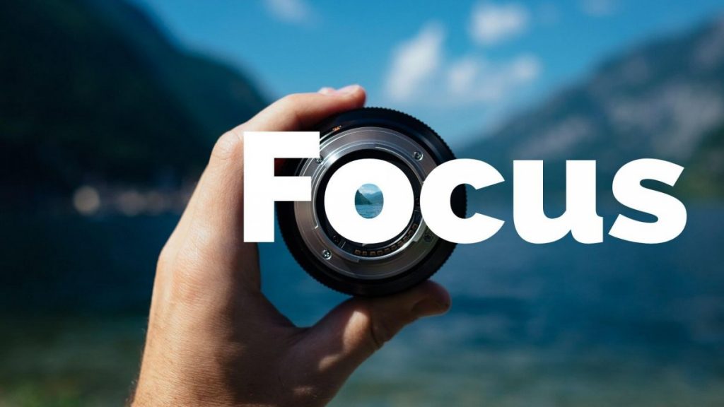 The word Focus over a camera lens held up against a blue mountain lake